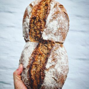 Eine Person präsentiert einen SYLTER TREBERBROT vor einer Backsteinmauer.