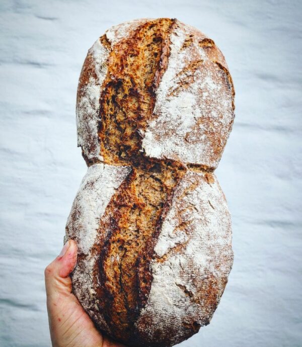 Bio_sylter_Treber_Brot-Sauerteig-Watt-Bier_Lund-sylt.jpg Eine Person präsentiert einen SYLTER TREBERBROT vor einer Backsteinmauer.