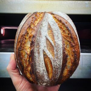 Eine Person hält ein JOGHURT-SAUERTEIGBROT 500g vor einen Ofen.